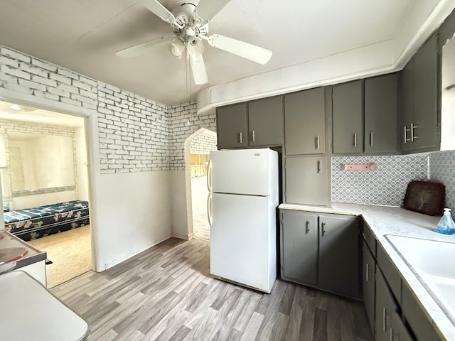 kitchen with light wood-type flooring, tasteful backsplash, ceiling fan, sink, and white fridge