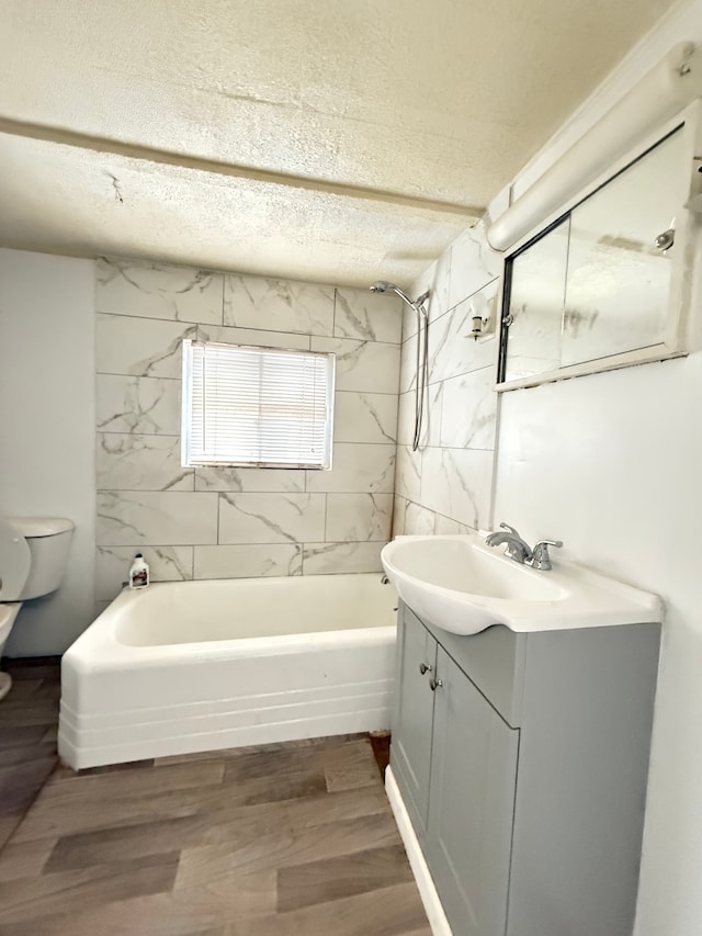 full bathroom with tiled shower / bath combo, a textured ceiling, toilet, vanity, and hardwood / wood-style flooring