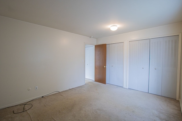 unfurnished bedroom featuring multiple closets and light colored carpet