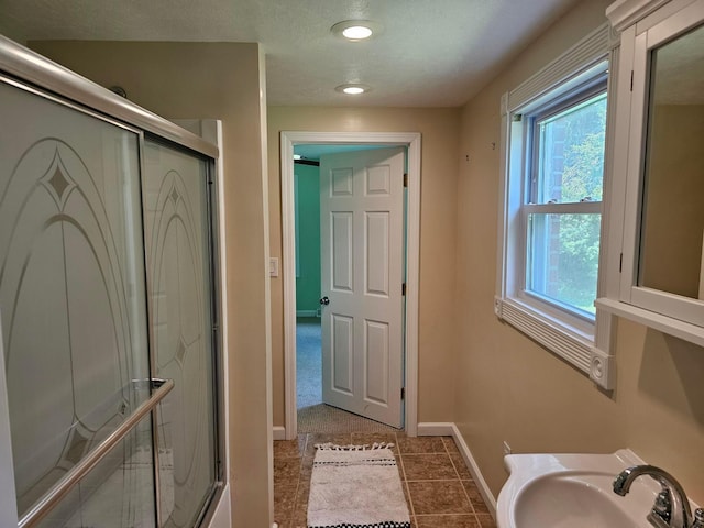 bathroom with a textured ceiling, tile patterned floors, a shower with door, and sink