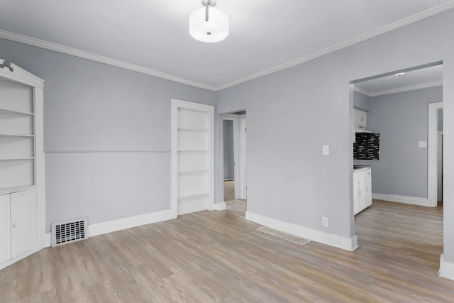 spare room featuring built in shelves, light wood-type flooring, and crown molding