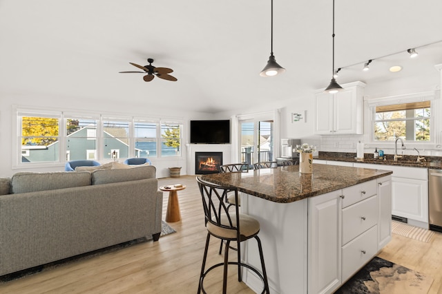 kitchen with light hardwood / wood-style floors, white cabinetry, a healthy amount of sunlight, and dark stone countertops