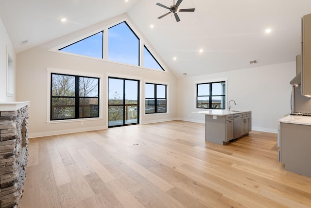 unfurnished living room featuring a fireplace, light hardwood / wood-style flooring, high vaulted ceiling, and plenty of natural light