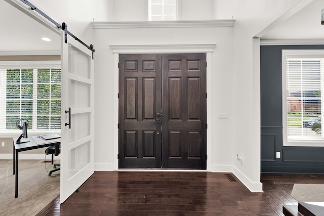 entrance foyer with a barn door, dark hardwood / wood-style flooring, and ornamental molding