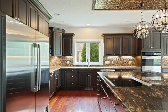 kitchen featuring decorative backsplash, stainless steel appliances, dark wood-type flooring, an inviting chandelier, and hanging light fixtures