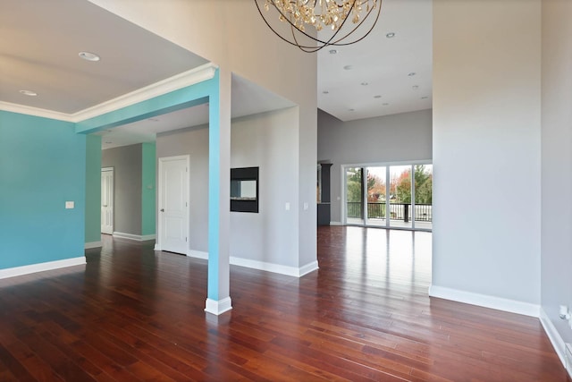 empty room with a towering ceiling, dark wood-type flooring, a notable chandelier, and ornamental molding