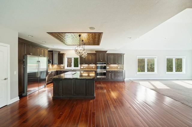 kitchen with dark wood-type flooring, a kitchen island, hanging light fixtures, and appliances with stainless steel finishes