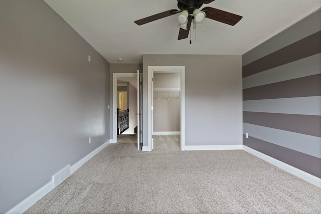 unfurnished bedroom with a closet, a walk in closet, light colored carpet, and ceiling fan