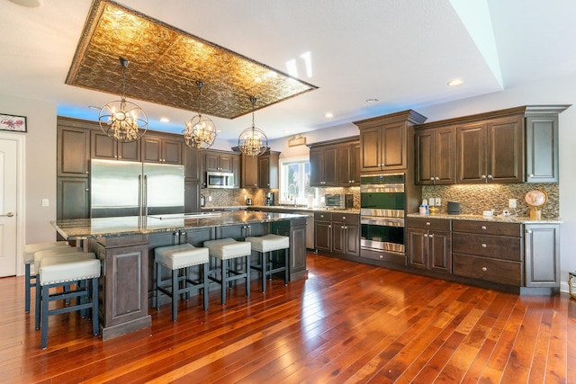 kitchen with dark hardwood / wood-style flooring, backsplash, stainless steel appliances, a spacious island, and hanging light fixtures