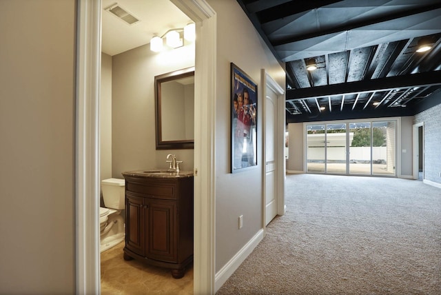 corridor with beamed ceiling, light colored carpet, and sink