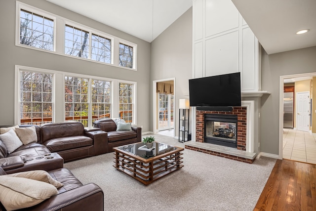 living room with wood-type flooring, high vaulted ceiling, a brick fireplace, and a wealth of natural light