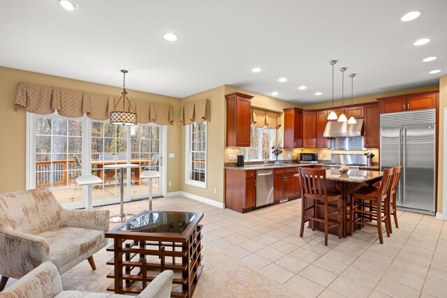 kitchen featuring light tile patterned floors, exhaust hood, decorative light fixtures, and appliances with stainless steel finishes