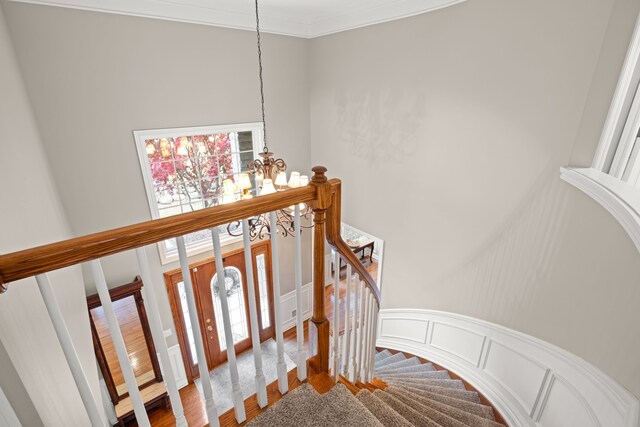 stairs featuring hardwood / wood-style floors, ornamental molding, and a chandelier