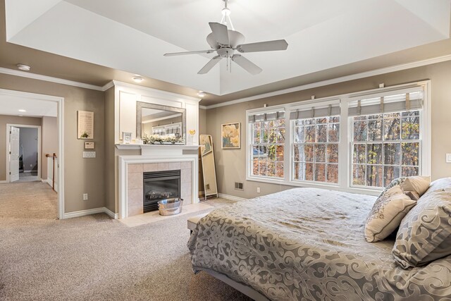 carpeted bedroom featuring ceiling fan, crown molding, a tile fireplace, and a tray ceiling