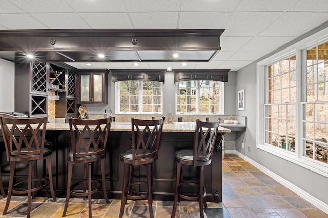 bar with a paneled ceiling and light stone countertops