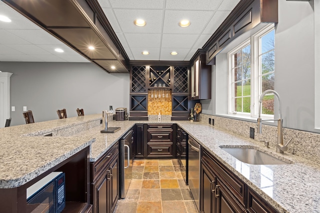 kitchen with black microwave, sink, light stone counters, stainless steel dishwasher, and a breakfast bar area