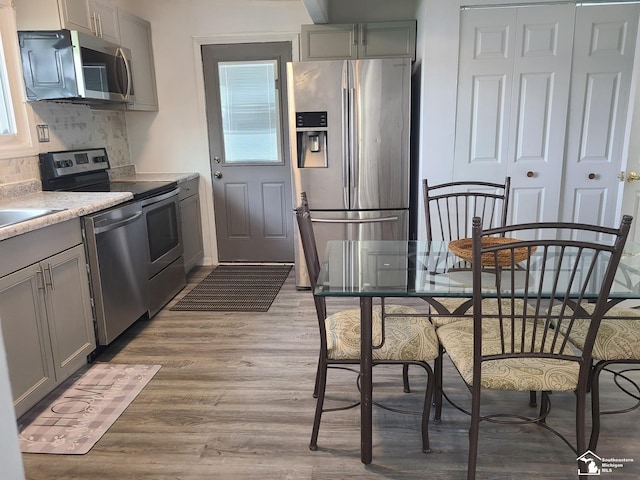 kitchen featuring backsplash, gray cabinetry, light wood-type flooring, and appliances with stainless steel finishes