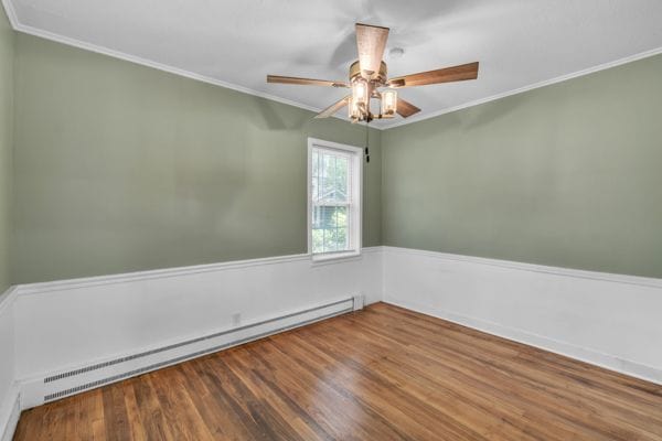 empty room with hardwood / wood-style flooring, ceiling fan, crown molding, and baseboard heating