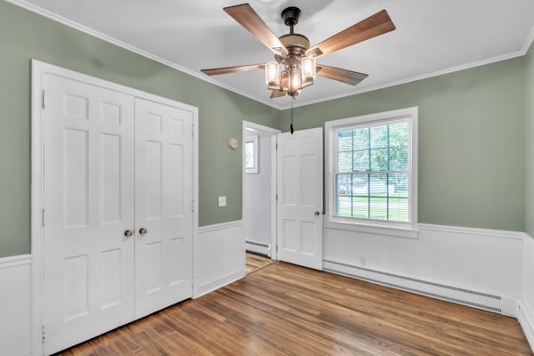 unfurnished bedroom with hardwood / wood-style floors, a closet, baseboard heating, and ceiling fan