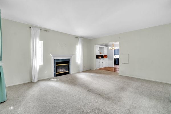 unfurnished living room featuring a fireplace, carpet floors, and a chandelier