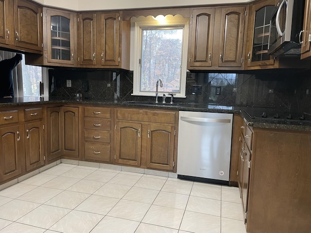 kitchen featuring sink, backsplash, dark stone counters, light tile patterned floors, and appliances with stainless steel finishes