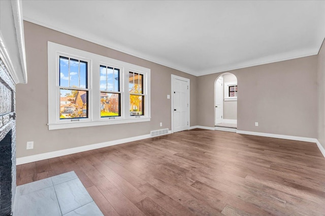 unfurnished living room featuring hardwood / wood-style flooring, a stone fireplace, and crown molding