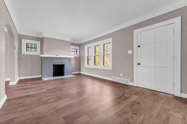 unfurnished living room featuring wood-type flooring, a brick fireplace, and crown molding