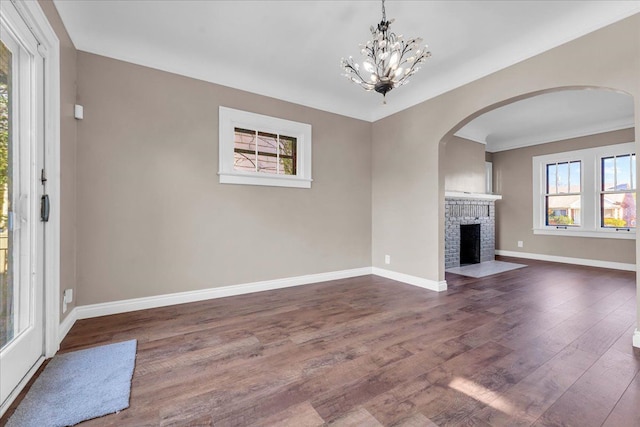 unfurnished living room featuring dark hardwood / wood-style flooring, an inviting chandelier, a brick fireplace, and ornamental molding