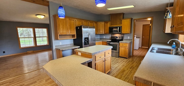 kitchen featuring stainless steel appliances, sink, decorative light fixtures, light hardwood / wood-style floors, and a kitchen island