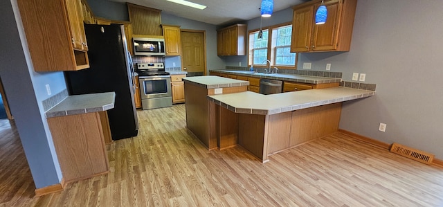 kitchen featuring lofted ceiling, sink, light hardwood / wood-style flooring, appliances with stainless steel finishes, and kitchen peninsula