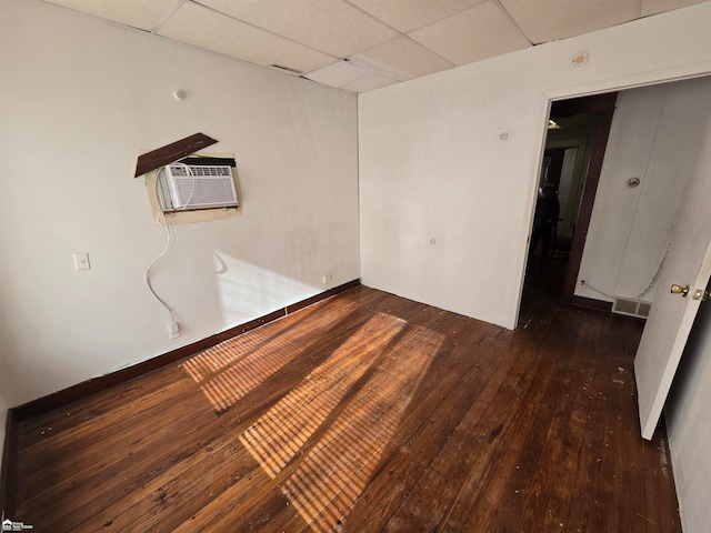 unfurnished room featuring dark hardwood / wood-style flooring, a drop ceiling, and a wall mounted AC