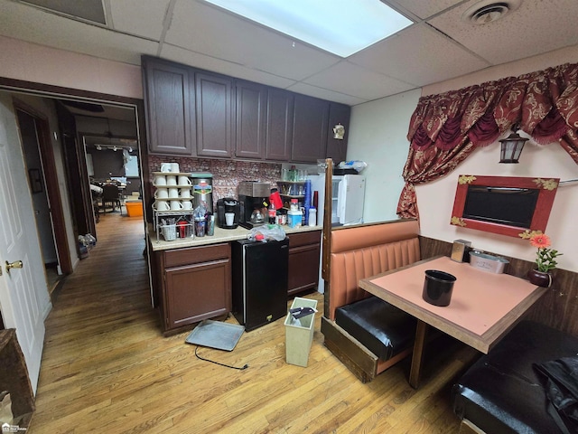 kitchen with a paneled ceiling, dark brown cabinets, black fridge, and light hardwood / wood-style flooring