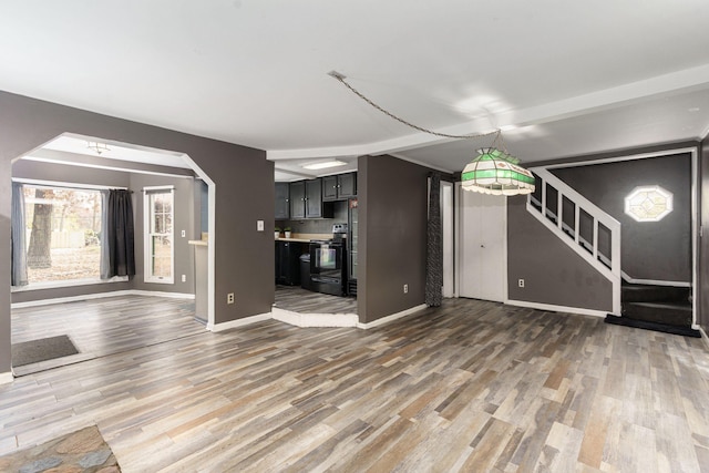 unfurnished living room with baseboards, stairway, arched walkways, and wood finished floors