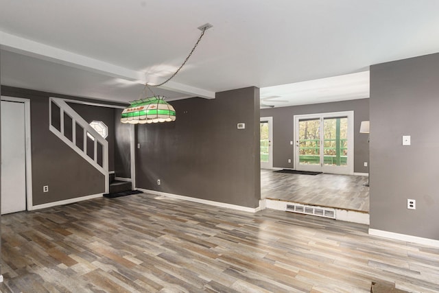 empty room with baseboards, visible vents, stairway, wood finished floors, and beam ceiling