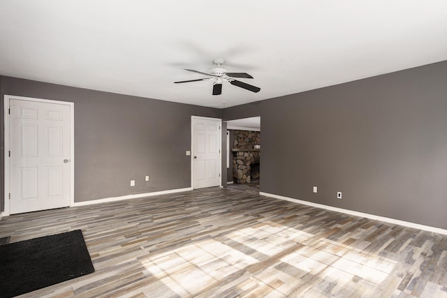 unfurnished room with a stone fireplace, ceiling fan, and hardwood / wood-style floors