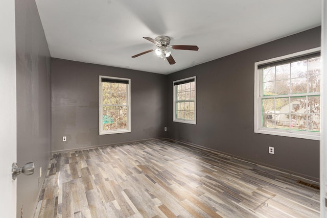 empty room with a wealth of natural light, ceiling fan, and light hardwood / wood-style floors