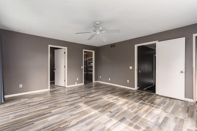 unfurnished bedroom featuring a walk in closet, a closet, light hardwood / wood-style flooring, and ceiling fan