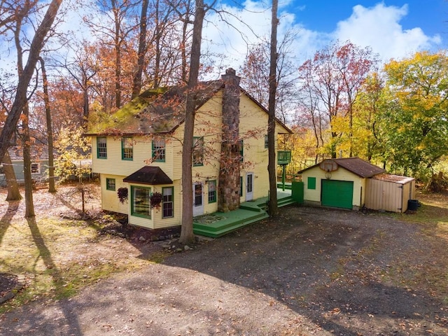 view of side of property with driveway, a garage, a chimney, and an outbuilding