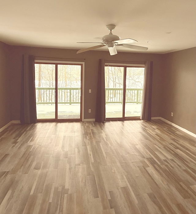 empty room with baseboards, light wood-style floors, a ceiling fan, and a healthy amount of sunlight