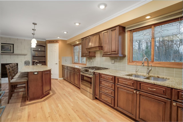 kitchen featuring pendant lighting, premium range hood, sink, high end stainless steel range oven, and light hardwood / wood-style flooring