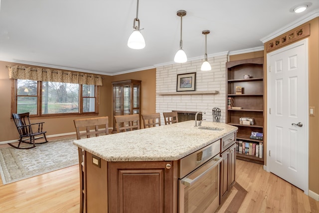 kitchen featuring sink, hanging light fixtures, light hardwood / wood-style floors, a center island with sink, and ornamental molding