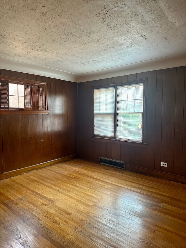 spare room with a textured ceiling, light hardwood / wood-style floors, and wooden walls