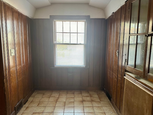 empty room featuring vaulted ceiling and wood walls