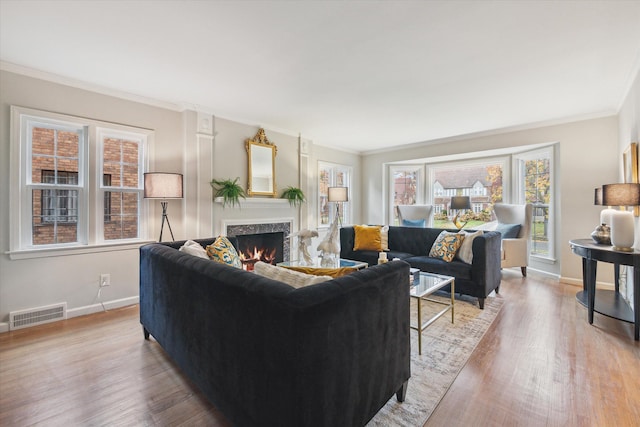 living room with a wealth of natural light, light hardwood / wood-style flooring, a high end fireplace, and ornamental molding