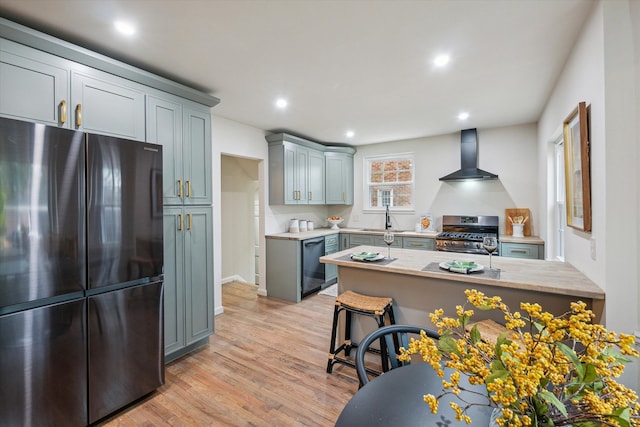 kitchen with gray cabinetry, wall chimney range hood, stainless steel appliances, and light hardwood / wood-style flooring