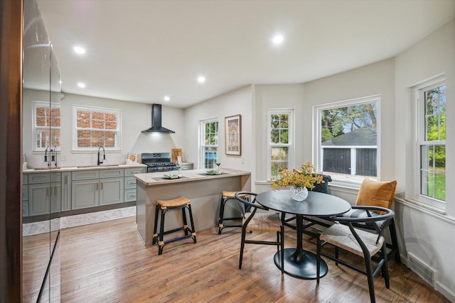 kitchen with stainless steel range with gas cooktop, sink, wall chimney range hood, light hardwood / wood-style flooring, and a breakfast bar area