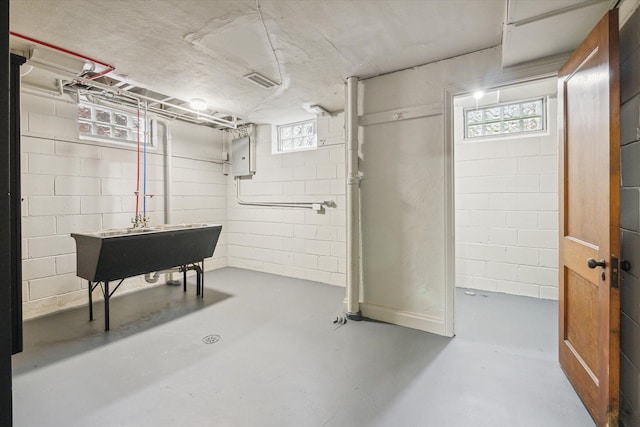 basement featuring electric panel, plenty of natural light, and sink