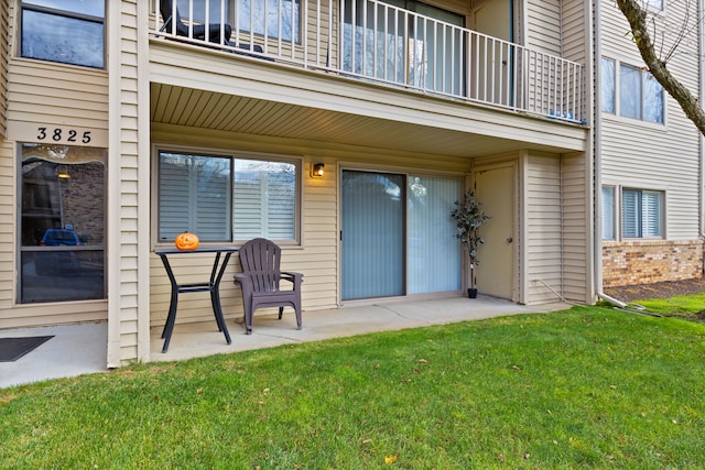 entrance to property with a balcony, a patio area, and a lawn