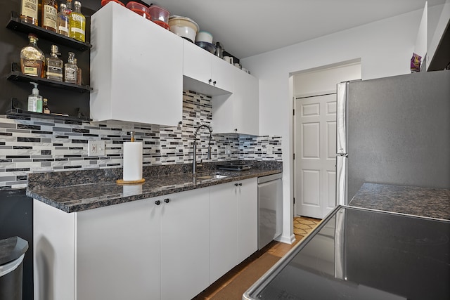 kitchen with decorative backsplash, dark stone counters, stainless steel appliances, sink, and white cabinetry