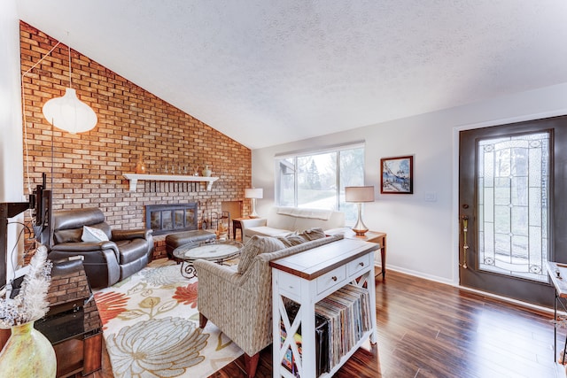 living room with dark wood-type flooring, vaulted ceiling, a brick fireplace, a textured ceiling, and brick wall